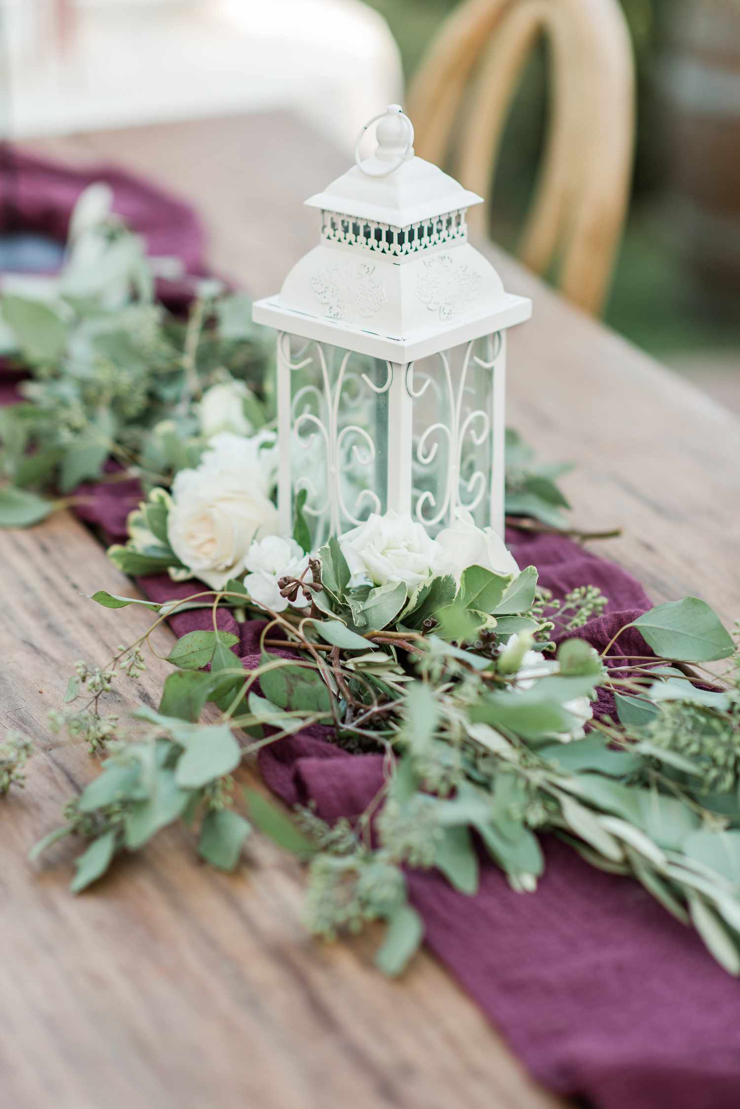 white lantern with greenery, white flowers, and purple tablecloth