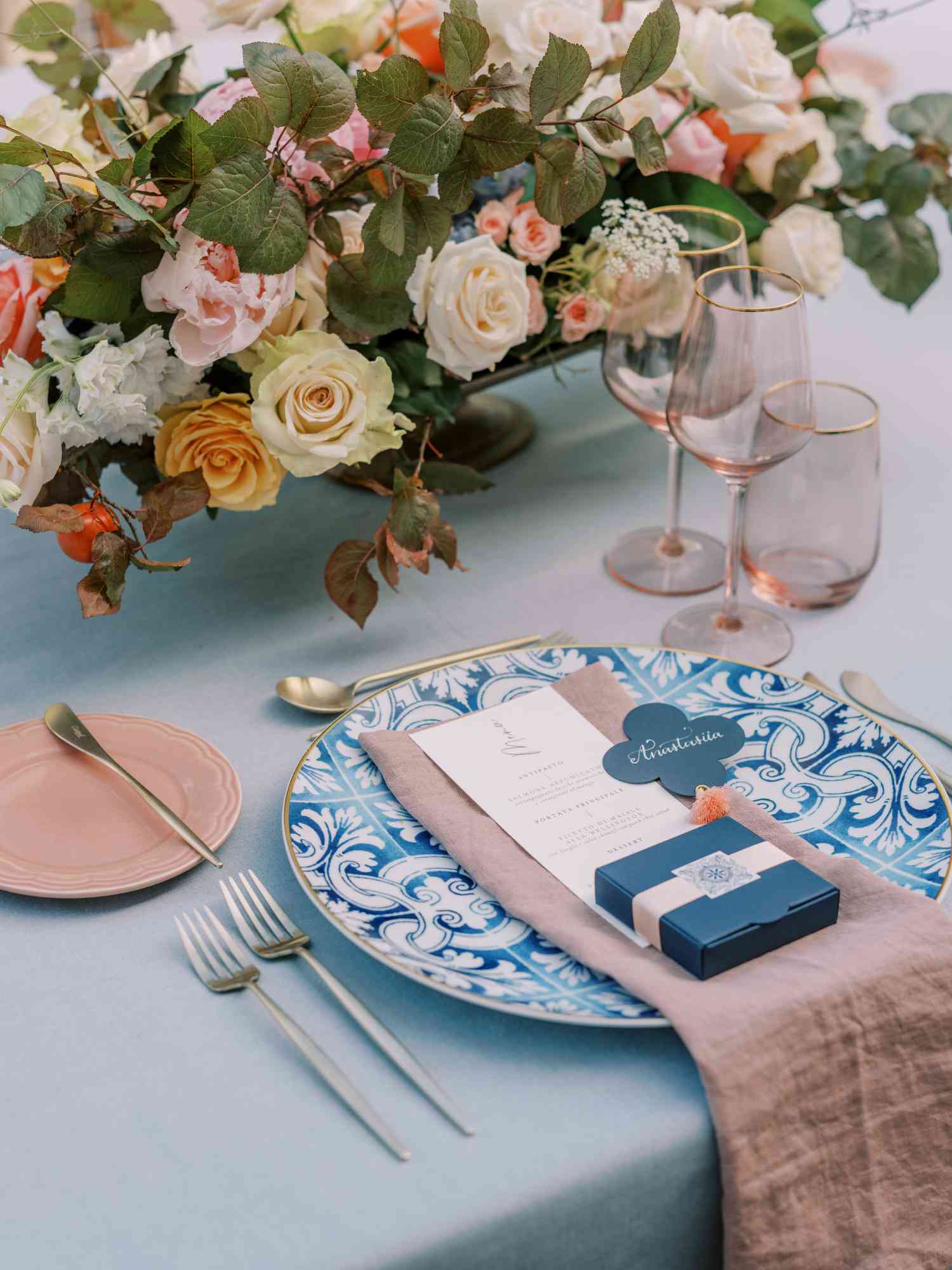 Place settings with blue tile-inspired chargers, dusty pink linens, pink glassware, and floral arrangements