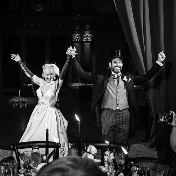 black and white photo of bride and groom holding hands while dressed in a masquerade theme wedding attire