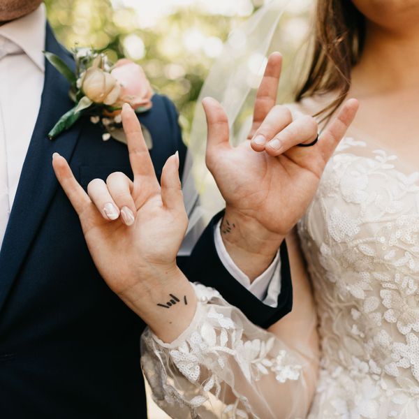 Closeup of Bride and Groomâs Interlocking Arms With Tattoo on Wrist and Hands Making âI Love Youâ Sign