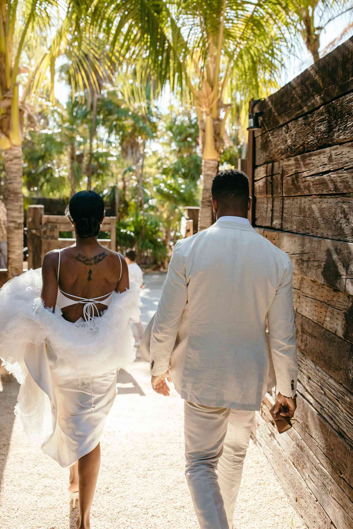 Couple Walks In Front of Palm Trees in Tulum, Mexico During Their Destination Wedding