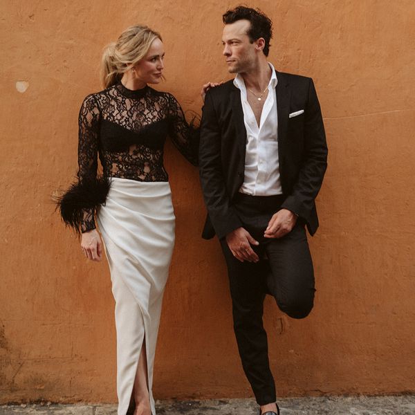 young woman wearing a black lace top and white skirt; young man wearing a black suit with an open collar button-down shirt