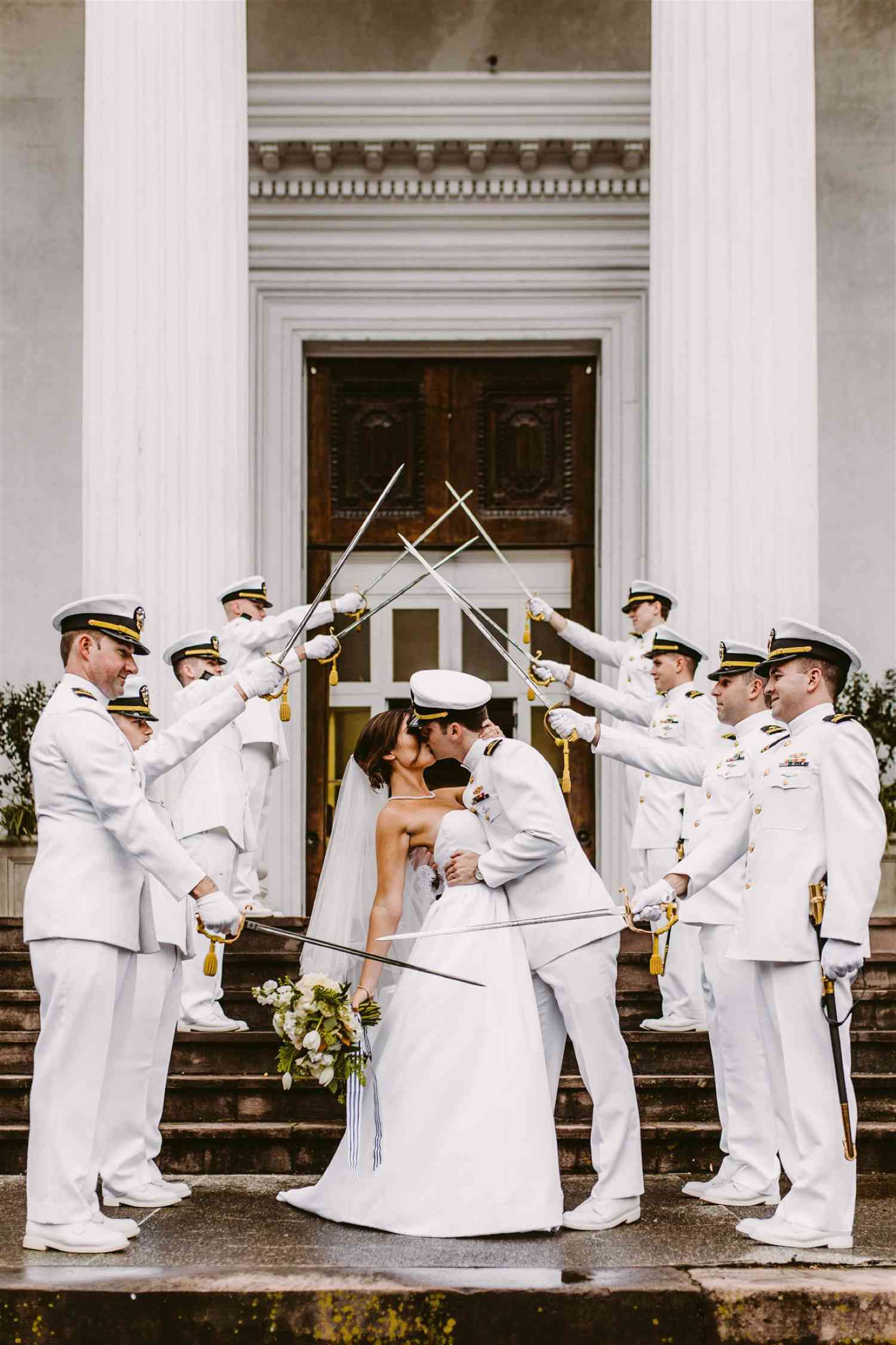Bride and groom kissing under a saber of swords on the stirs of a military wedding