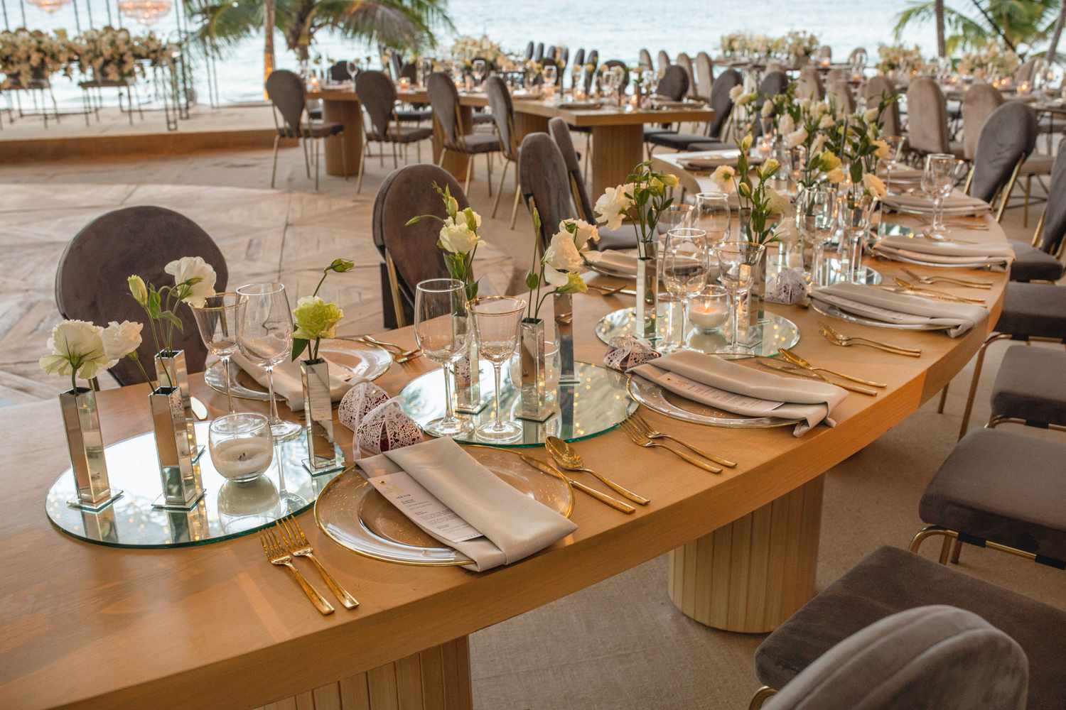 curved wood tables with gold flatware and mirrored floral arrangements