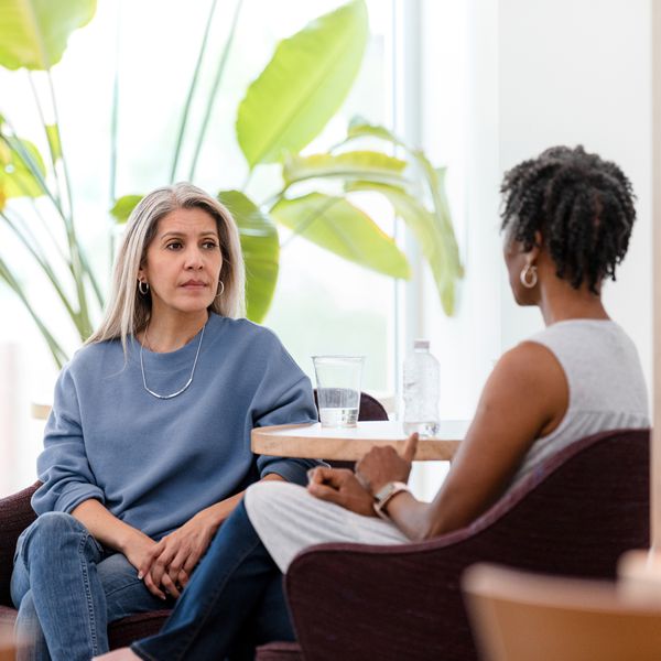 The mature adult woman has a serious look on her face as she listens to the unrecognizable female