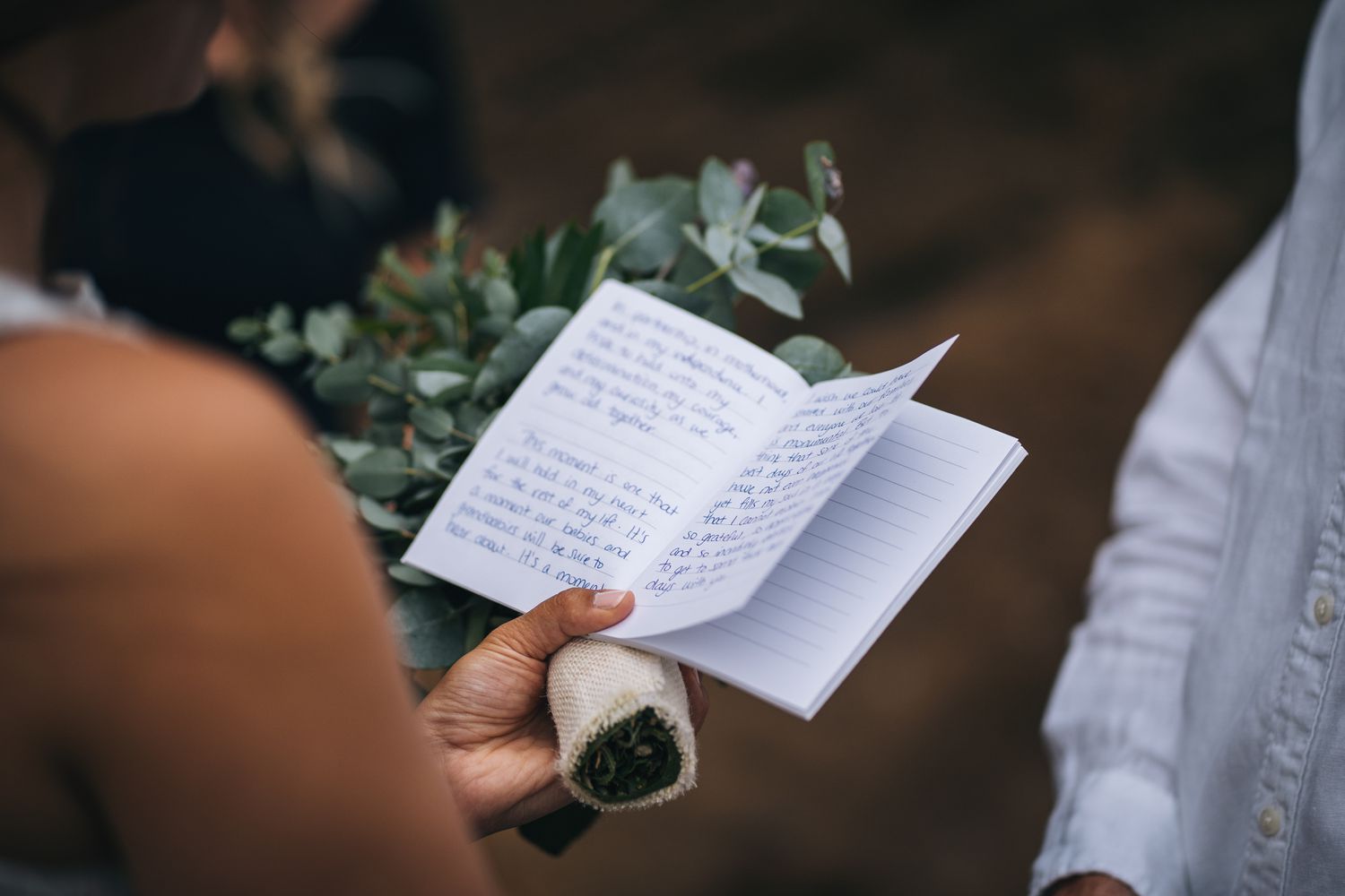 Closeup of Woman Holding Greenery Bouquet and Notebook With Handwritten Vows