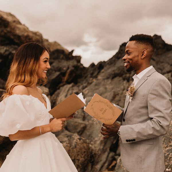 Smiling Bride and Groom Holding Vow Booklets With Mountain Backdrop Behind Them