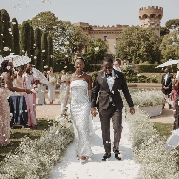 A bride and groom holding hands and smiling during the recessional while guests toss flower petals