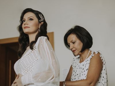 mother of the bride in white polka dot dress zipping up bride in bohemian wedding dress