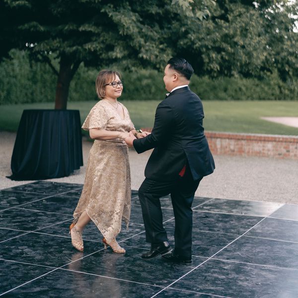 Groom in Black Tuxedo Dancing With Mother of the Groom in Gold Dress During Wedding Reception