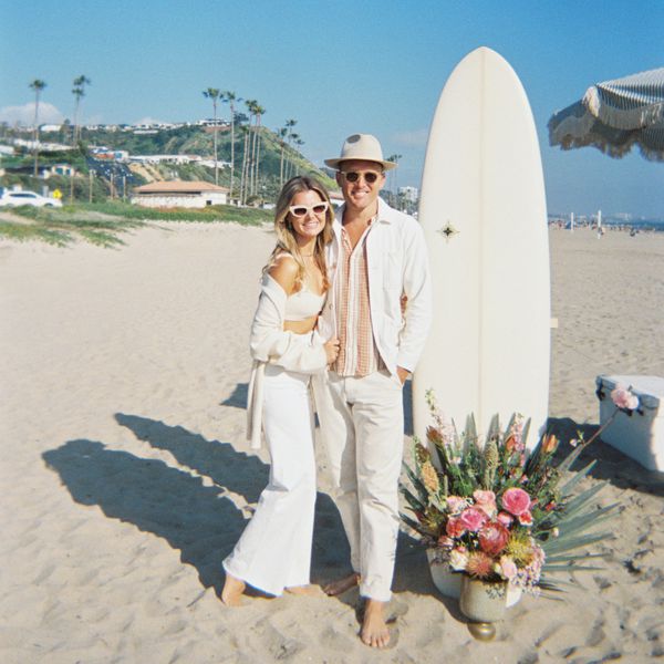 Bride and Groom at Beach Engagement Party Smiling in Front of Surfboard and Floral Arrangement