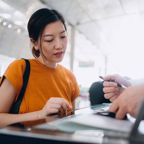 woman in orange t-shirt talking to employee at airline check-in counter about delayed flight