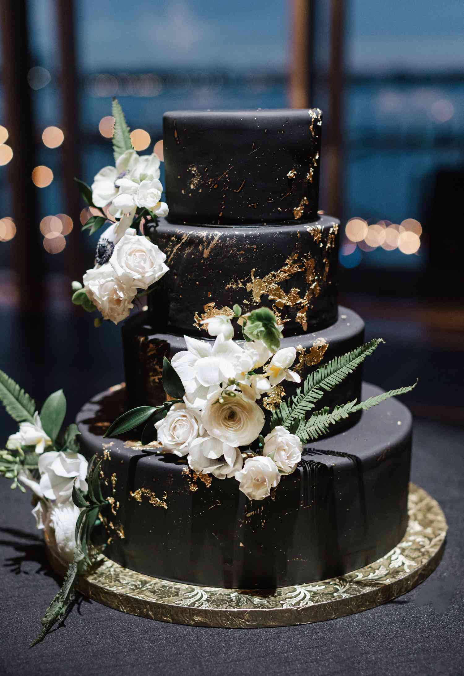 Four-tier black cake with gold leaf and white flowers