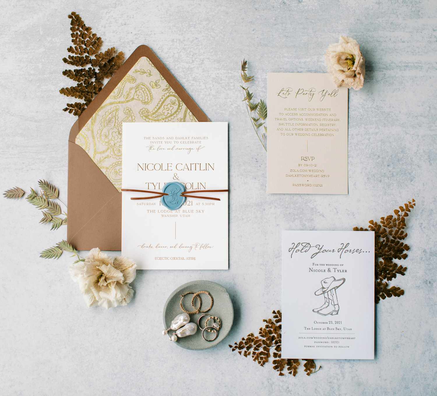 Invitation suite with brown envelope with paisley liner, a white invitation with a blue cowboy boot wax seal, neutral inserts, and cowboy boot illustrations