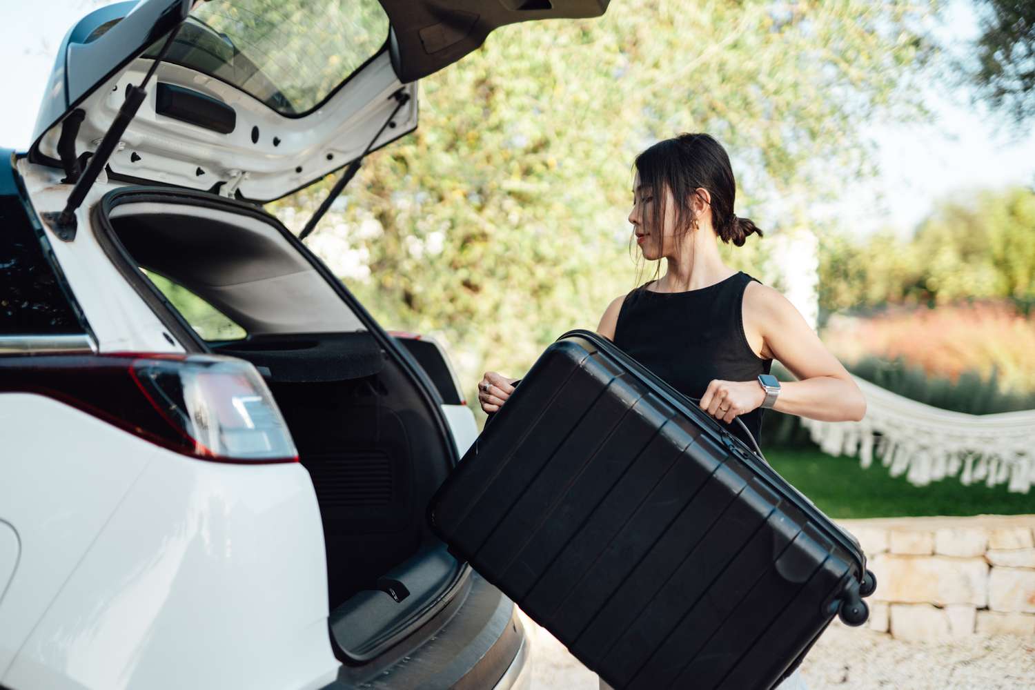 Woman putting black suitcase in trunk