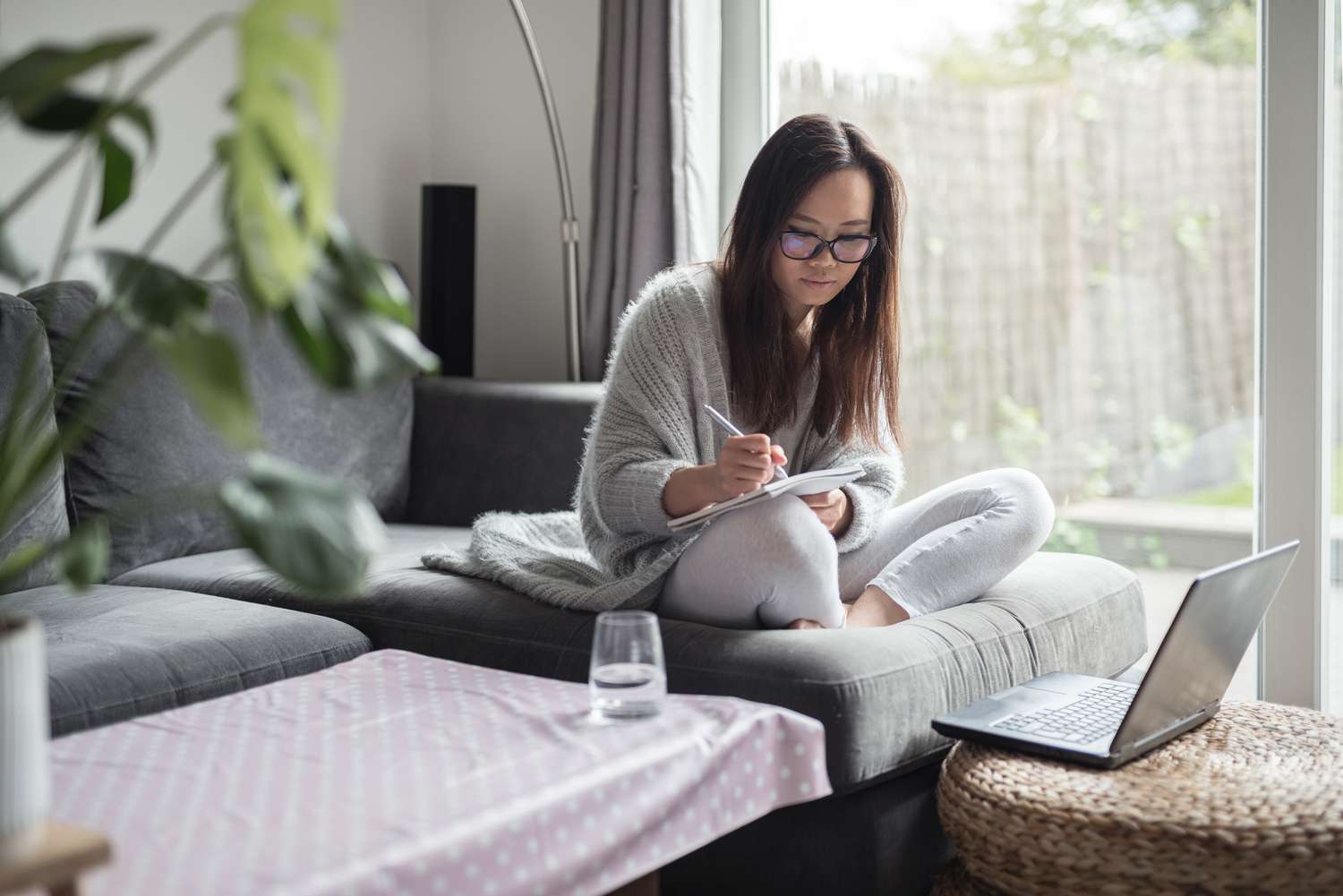 Woman sitting on a couch writing in a notebook with laptop open