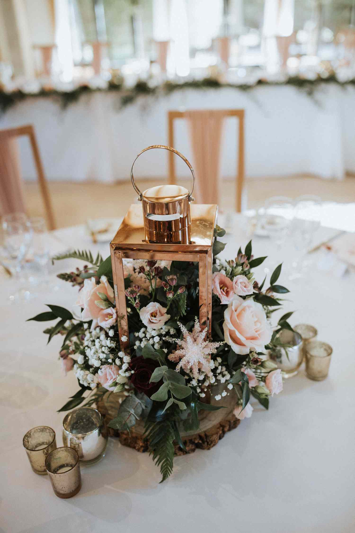 rose gold lantern with flowers spilling out on a white tablecloth