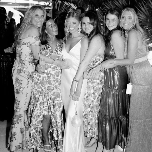 black and white photo of smiling bride and female wedding guests in long dresses holding purses and clutches.