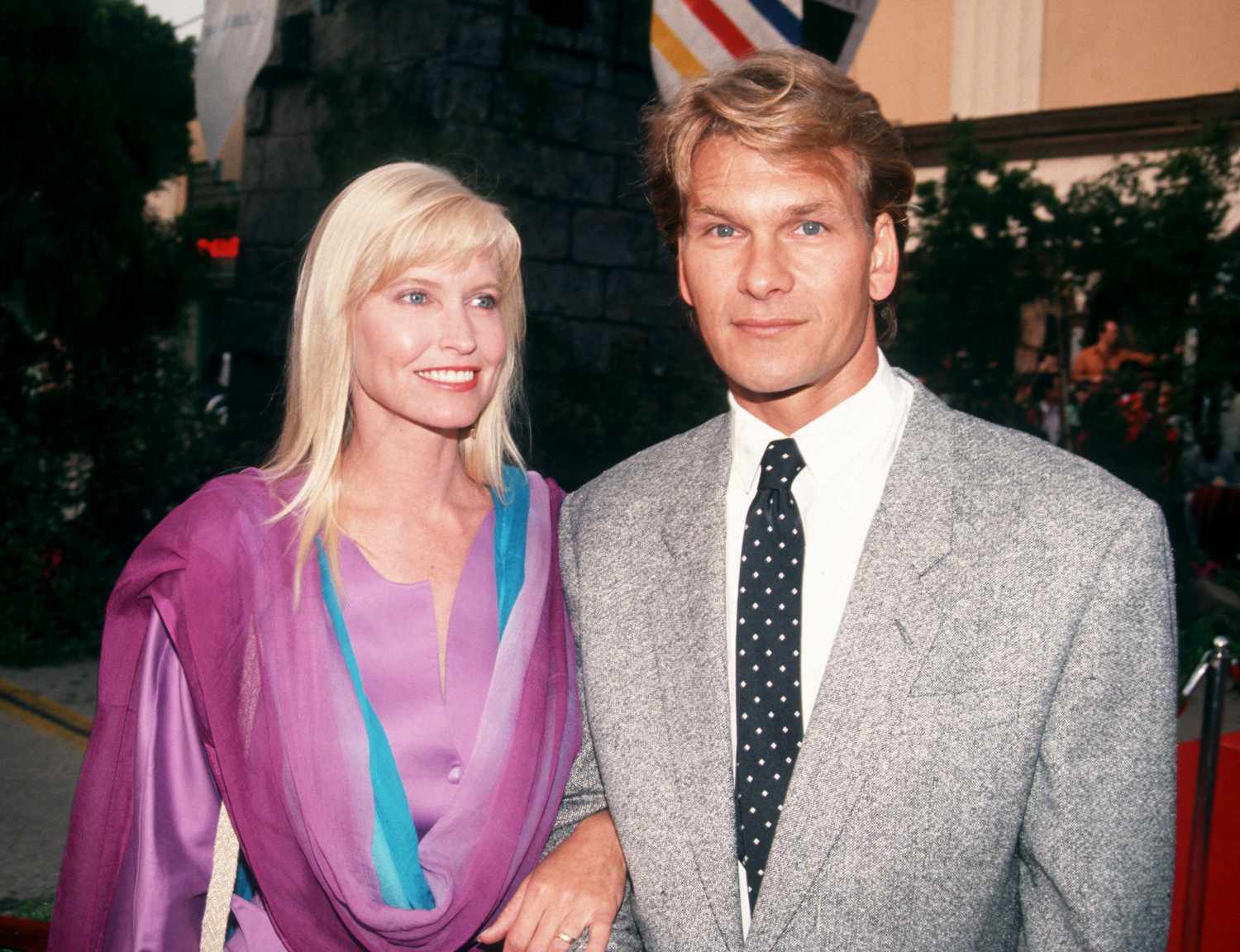 Young Patrick Swayze in Gray Suit and Black Polka Dot Tie and Lisa Niemi Swayze in Purple and Blue Dress in 1991