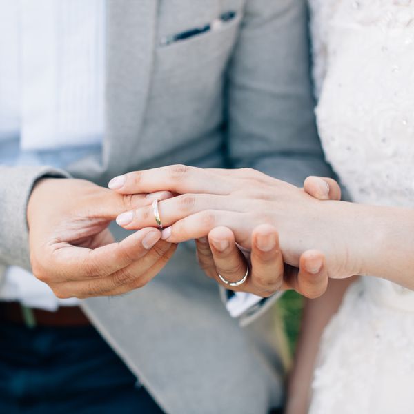 Closeup of Bride and Groomâs Hands As Groom Slips Gold Wedding Band on Brideâs Left Ring Finger