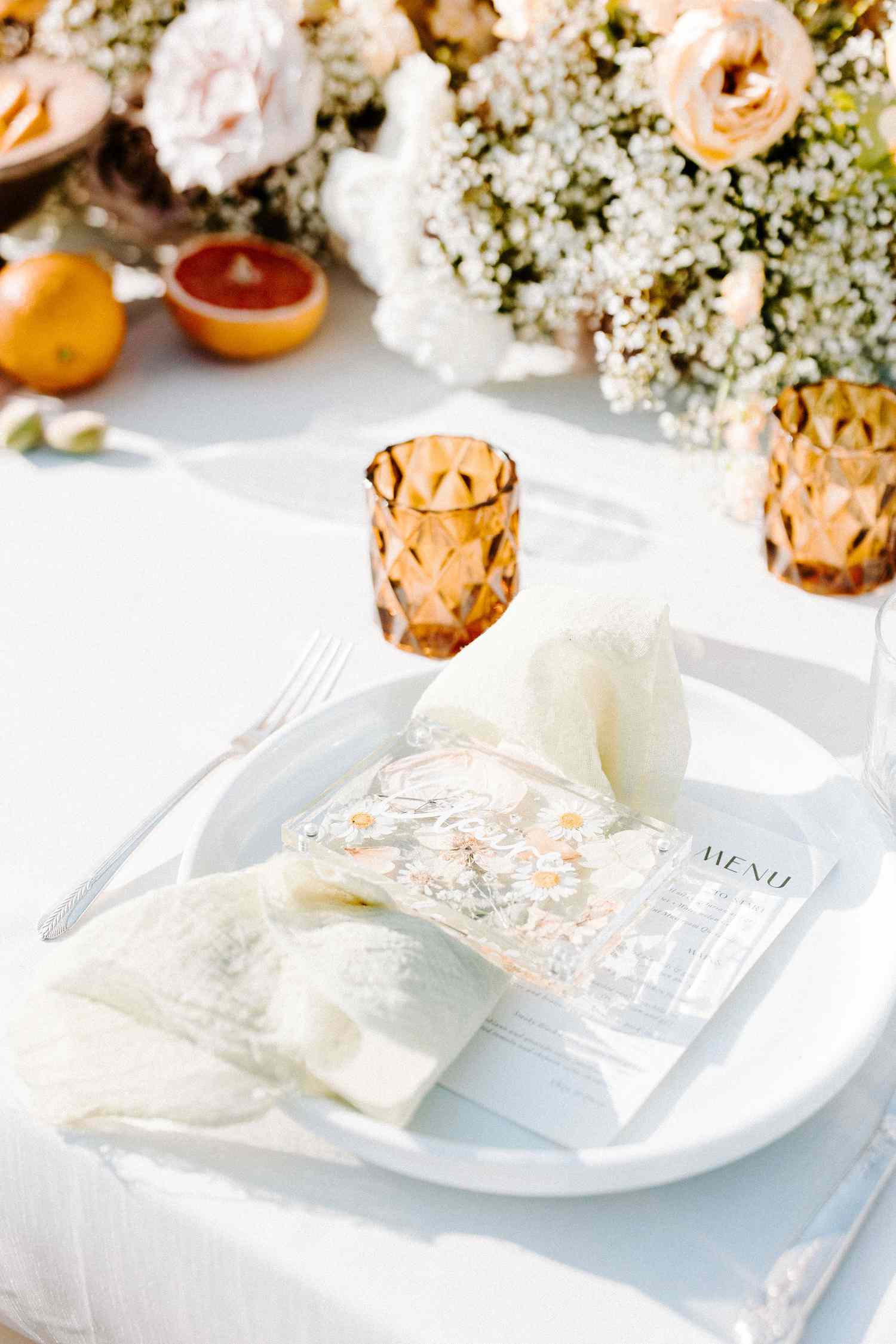 Wedding tablescape with white linens and plates, dried flower place cards. amber candles, and florals
