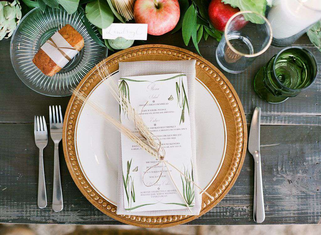 Place setting with gold charger, custom illustrated menu, wheat, and fruit centerpieces