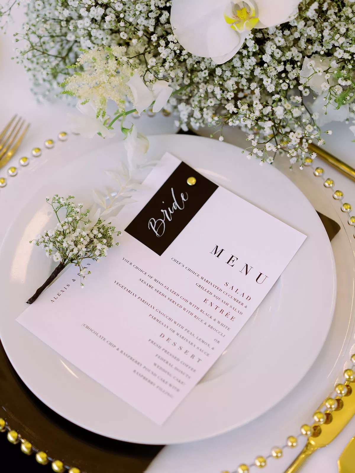 Tablescape with black and white menu, gold-accented chargers, and baby's breath arrangements