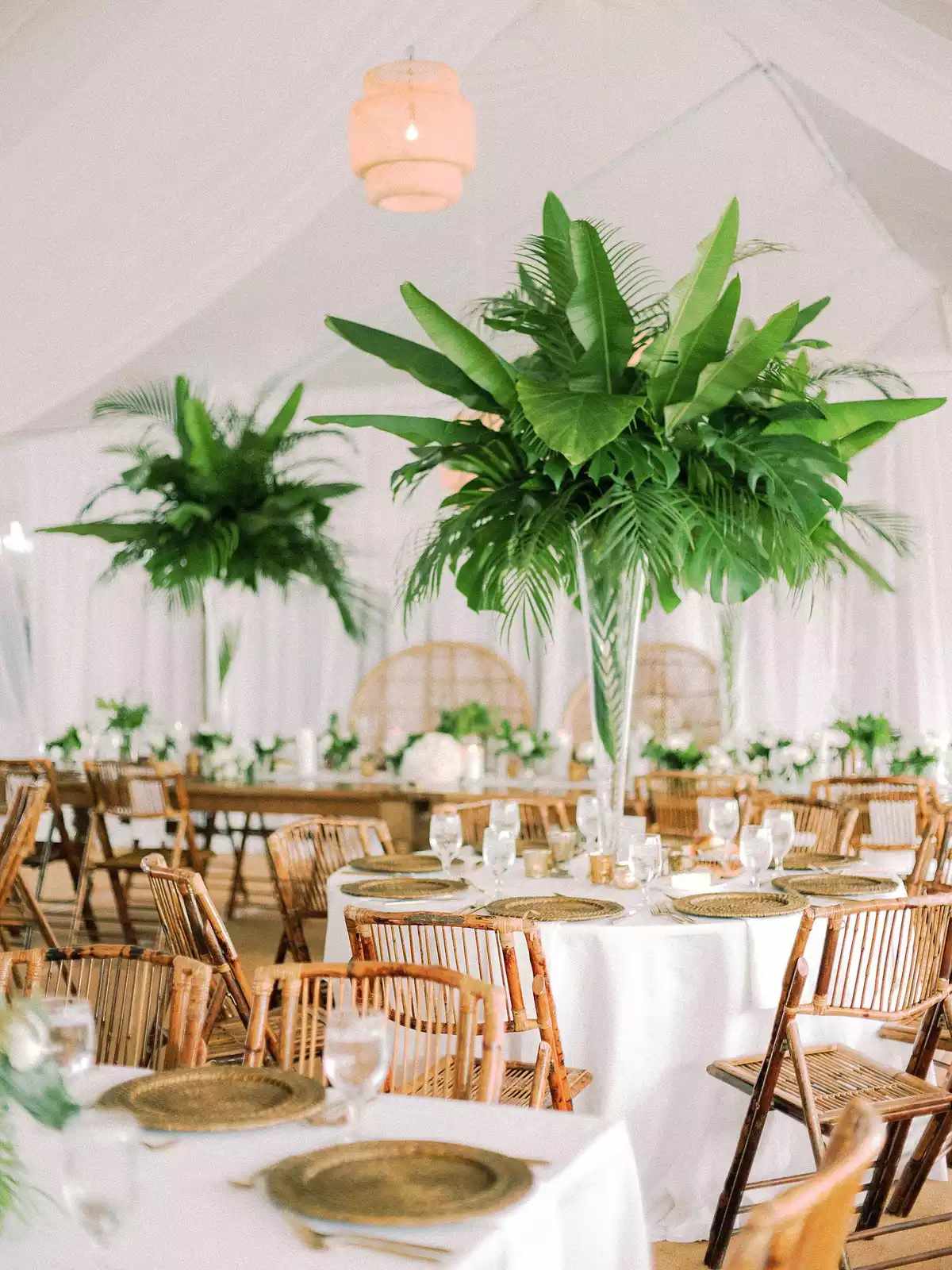 Translucent vases with monstera leave and palm leaves on round tables with white linens