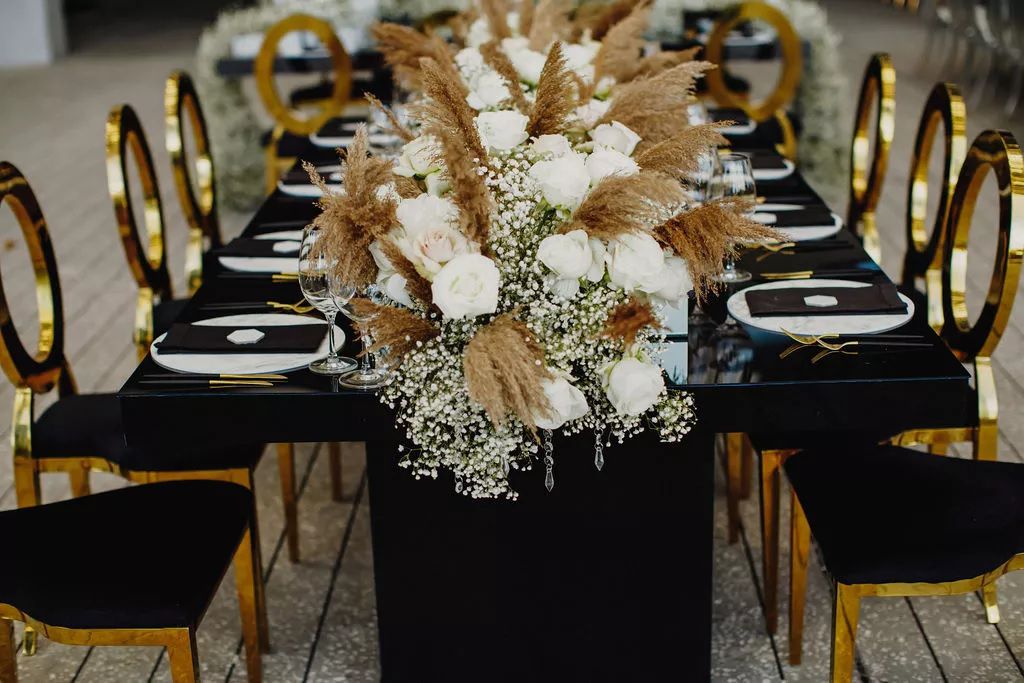 baby's breath table runner on black and gold wedding table with white florals, baby's breath, and pampa