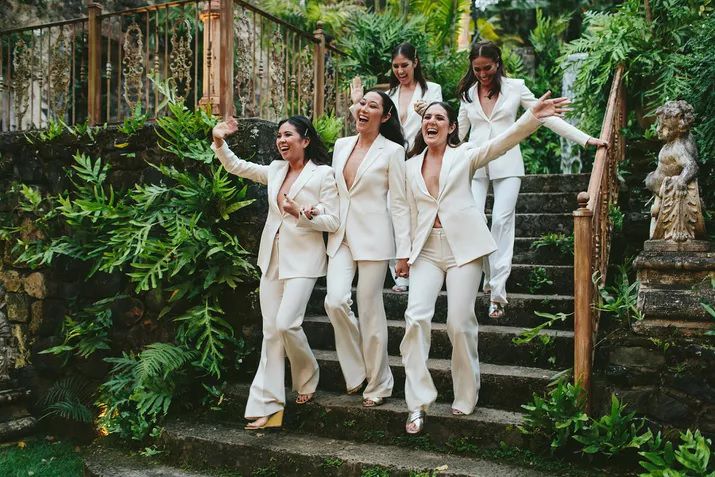 Bridal party in white suits walk down stairs for their wedding entrance