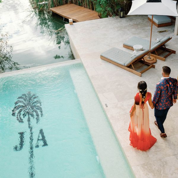 bride and groom in colorful attire walking next to pool with monogram