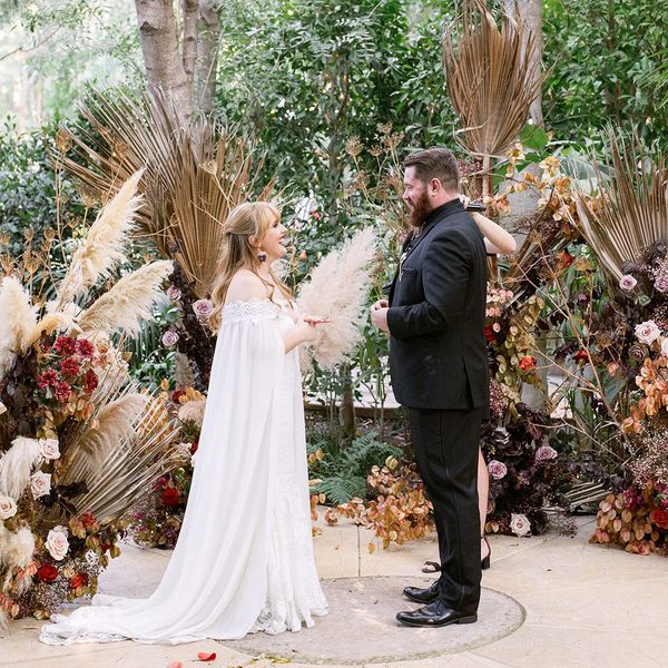 Bride and groom standing at the altar in front of dried palm leaves, pampas grass, and fall flowers during the ceremony