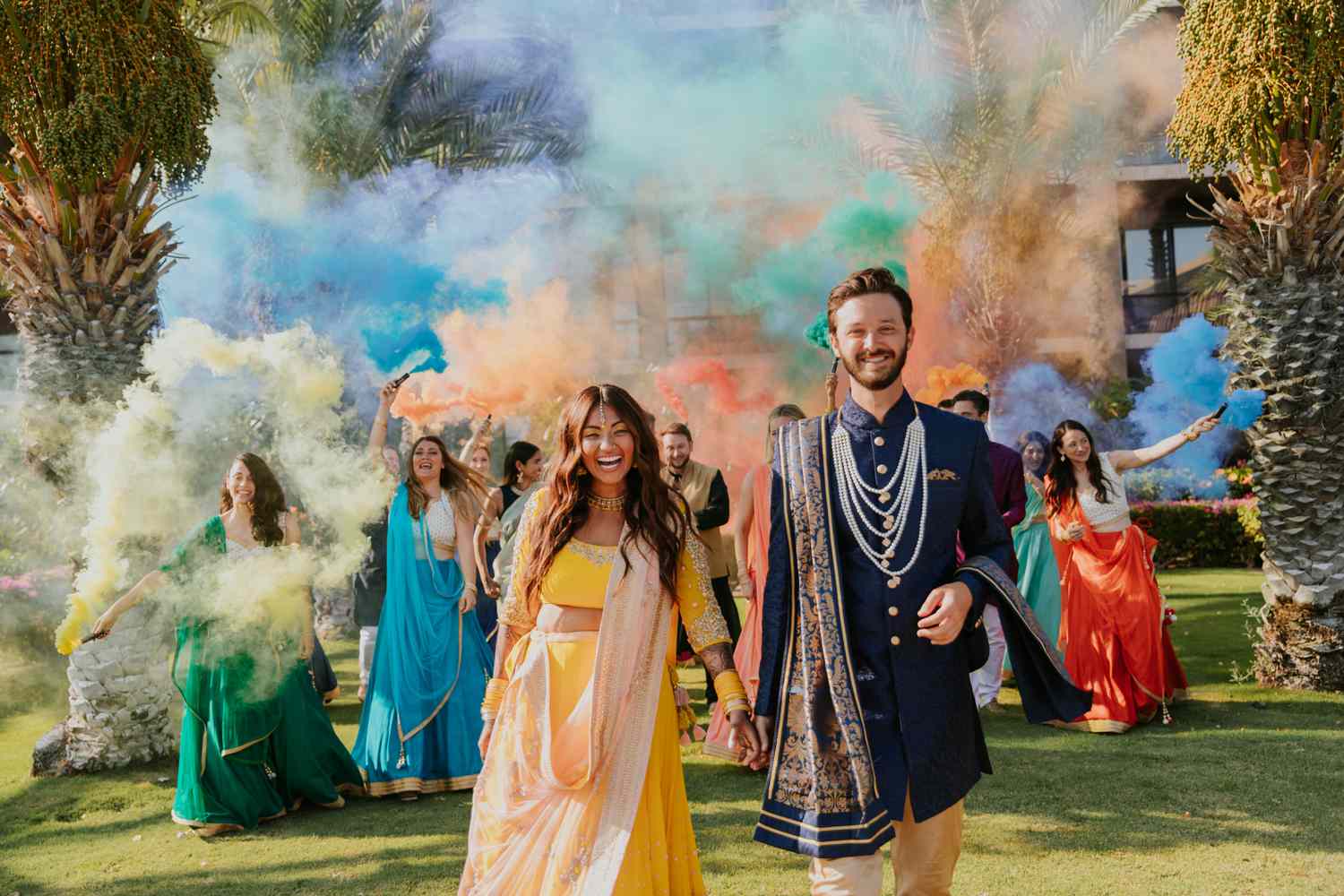 Wedding party releasing smoke bombs as the bride and groom, in Indian attire, walk in front of them