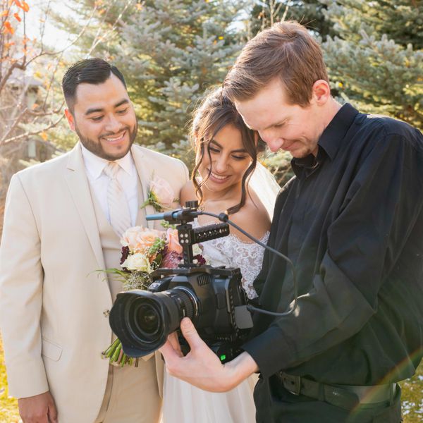 bride and groom look at videographer's camera