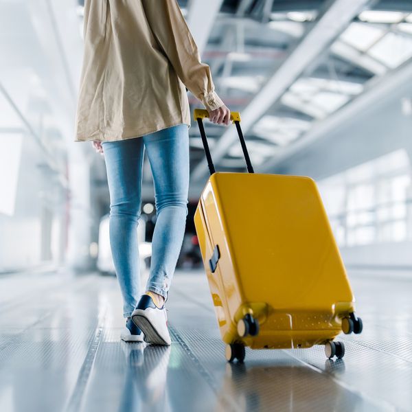 Lower Half of Woman in Jeans Rolling Yellow Suitcase Through the Airport