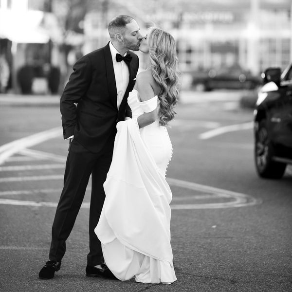 Black and White Image of Bride in Strapless Wedding Dress With Hair Down Kissing Groom in Tuxedo