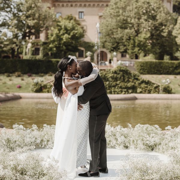 Bride and Groom Sharing First Kiss at Outdoor Wedding Ceremony with Castle Venue Behind Them