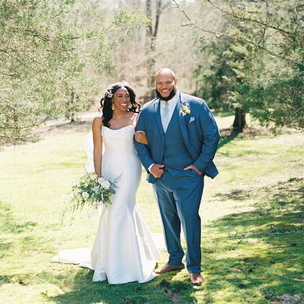 Bride in Wedding Dress with Hair Down Holding Bouquet Posing With Groom in Blue Suit on Grass