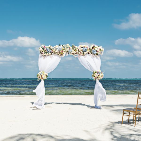 Arch With Flowers and Draped Curtains on Beach in Front of Ocean With Wooden Chiavari Chairs