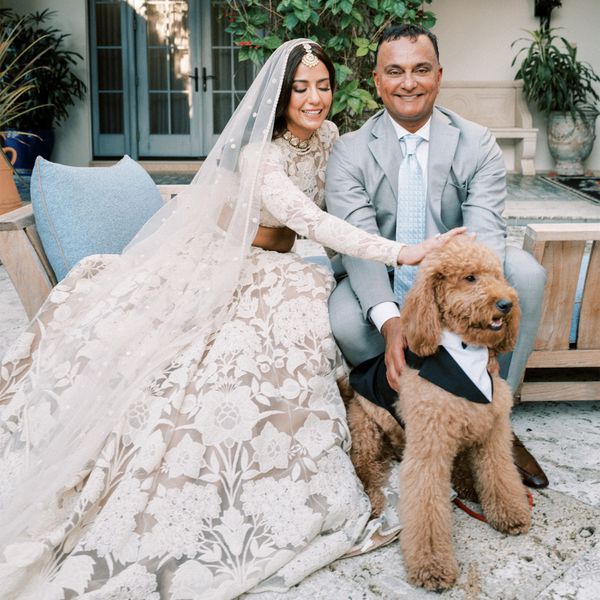 Bride in Two Piece Beige Floral Indian Wedding Dress Posing With Groom in Grey Suit and Dog in Tuxedo
