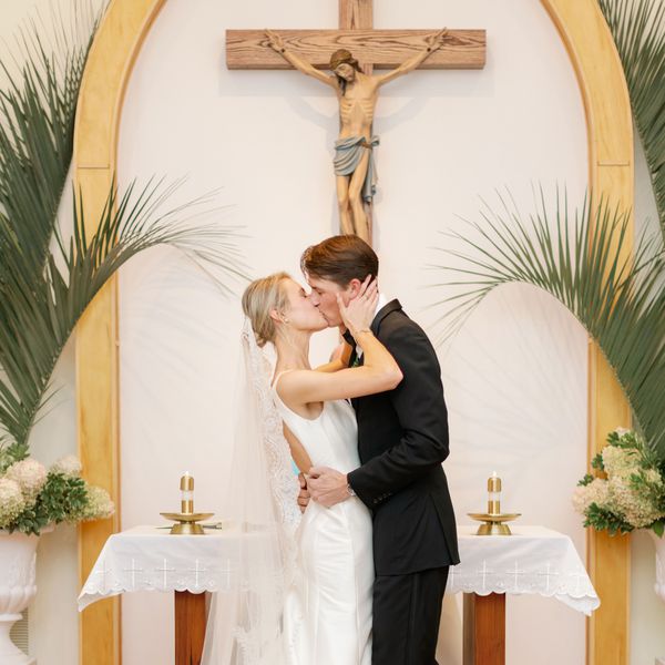 Bride and Groom Kissing in Front of Altar With Cross of Jesus, Palm Leaves, and Hydrangeas