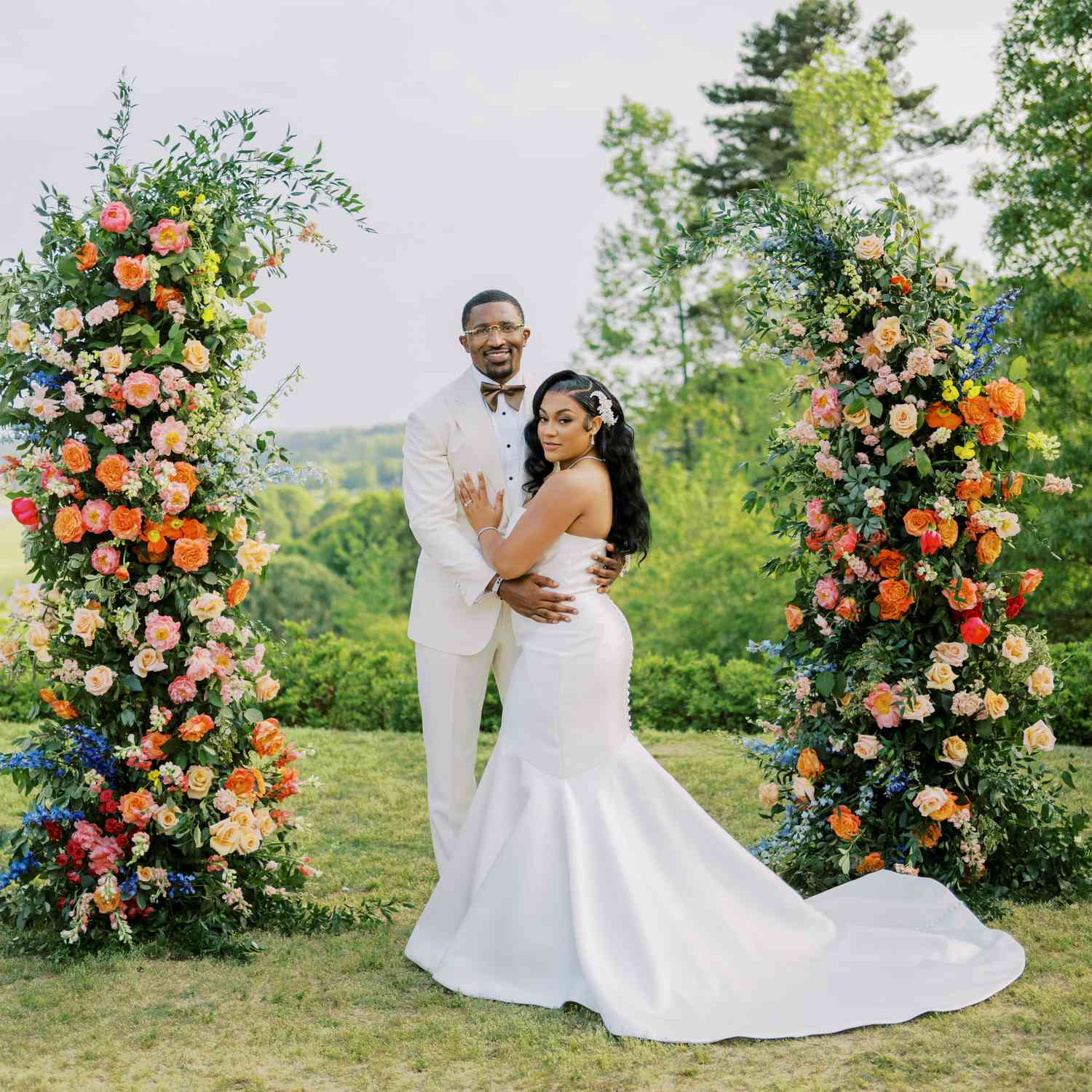 Bride in Strapless Wedding Dress Posing With groom in White Tuxedo at Altar With Colorful Flower Decor