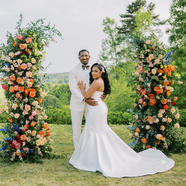 Bride in Strapless Wedding Dress Posing With groom in White Tuxedo at Altar With Colorful Flower Decor
