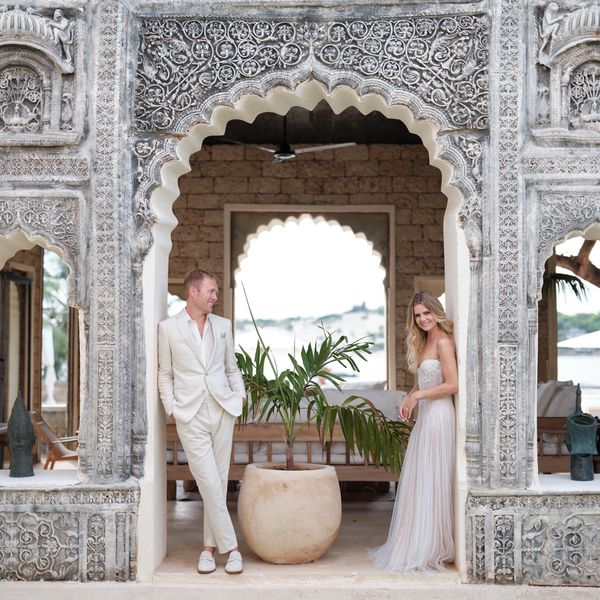 Bride In Strapless Wedding Dress Posing in Archway With Groom in Beige Suit