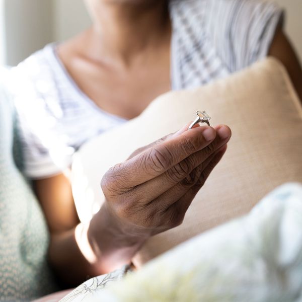 Closeup of Woman Holding Cushion-Cut Diamond Ring on Silver Band While Sitting on Couch