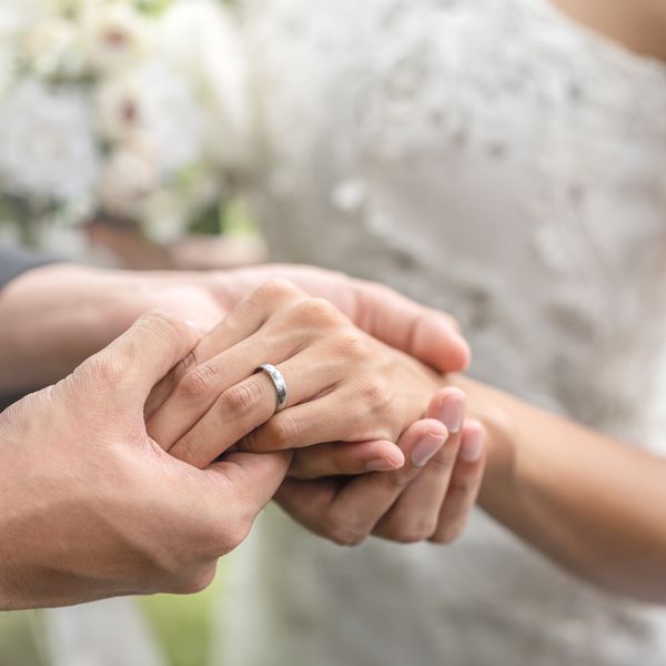 Bride and Groom Holding Hands in Wedding Ceremony With Silver Wedding Band on Bride's Finger
