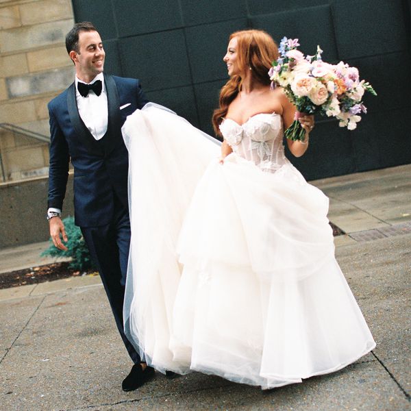 Bride in Strapless Wedding Dress Holding Bouquet Posing With Groom in Navy Tuxedo