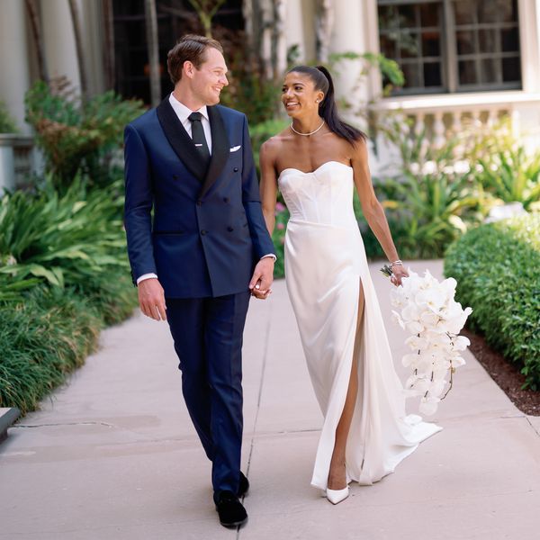 Bride in White Wedding Dress With Hair in Pony Tail Holding Hands With Groom in White Suit
