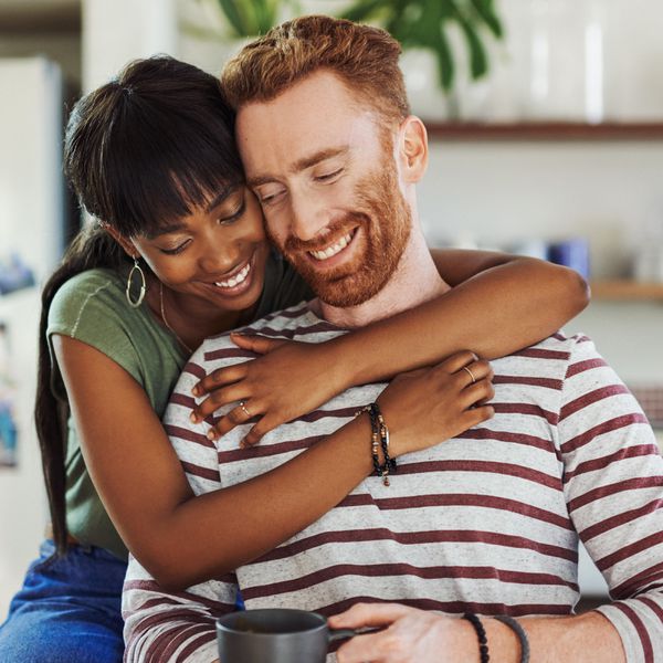 Brunette Woman Hugging Red-Headed Man From Behind in Home