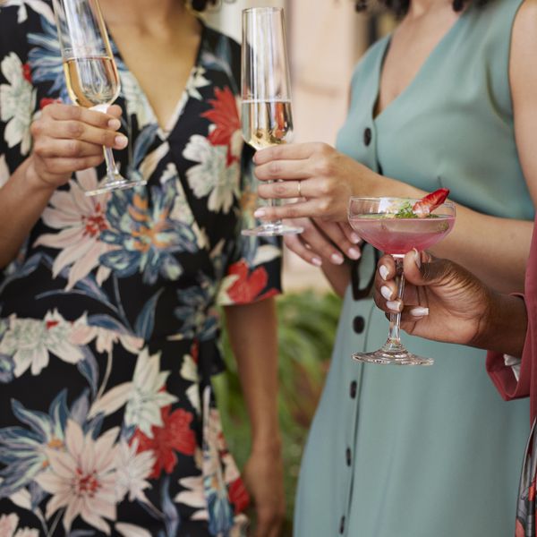 Closeup of Woman in Floral Wrap Dress and Blue Button-Down Dress Holding Champagne Coupes